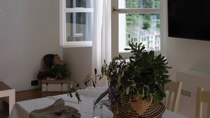 A room with a large window, a table with a plant, and a chair. - My Place Your Place - Corniglia, 5 Terre (Vernazza, Corniglia)