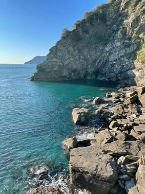 A rocky coastal landscape with clear turquoise water and a steep cliff.