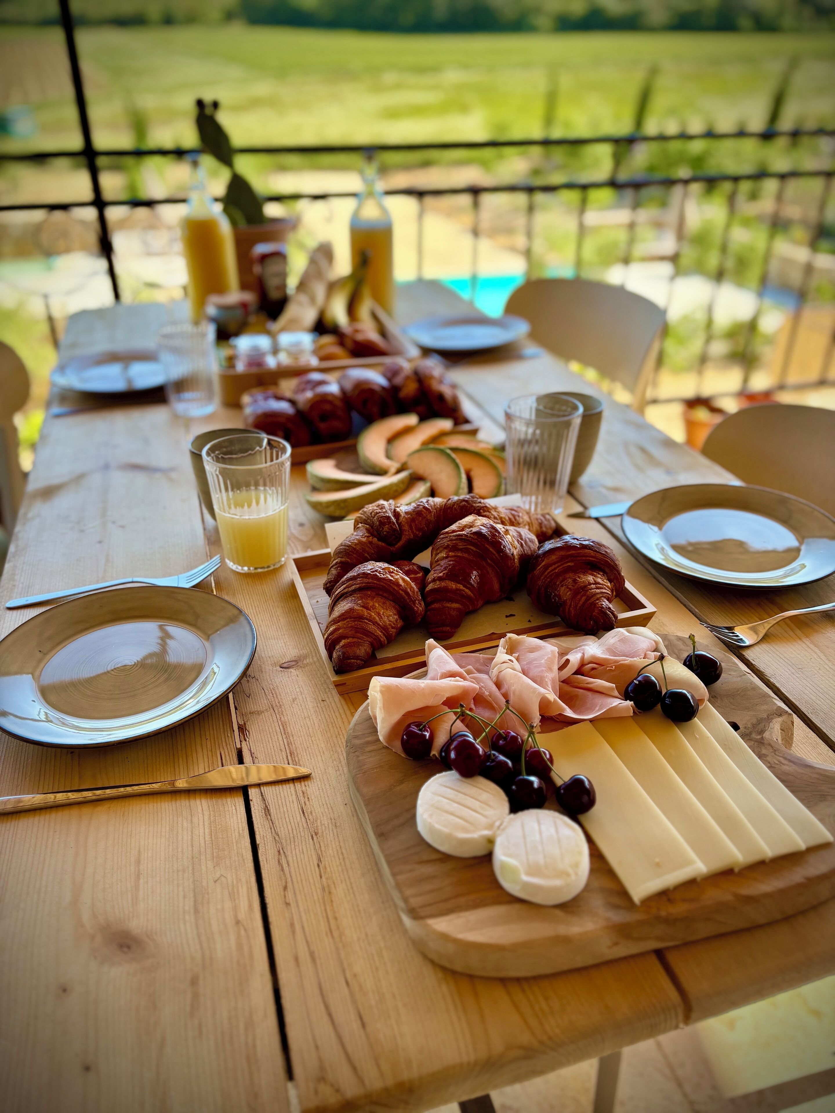 Una mesa de madera preparada para una comida con cruasanes, queso y frutas.
