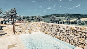 Una piscina infinita de piedra con agua cristalina, rodeada por una zona pavimentada y un muro de piedra.