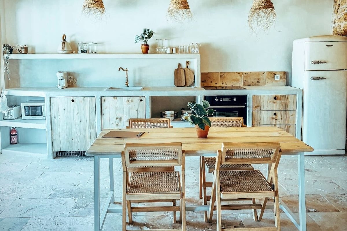A rustic kitchen with wooden beams, a central island, and hanging light fixtures.