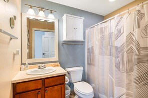 A bathroom with a white sink, mirror, and cabinet, a toilet, and a shower curtain with a geometric pattern. - Horseshoe Bay #1-Private Golf Club Access! (Egg Harbor)