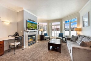 A living room with a fireplace, a television mounted above it, a sofa, a coffee table, and a large window providing a view of the outdoors. - Horseshoe Bay #1-Private Golf Club Access! (Egg Harbor)