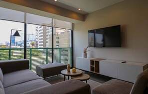 A modern living room with a large window, a flat-screen TV, and a minimalist furniture arrangement. - w* | Plaza Stays 2BR with Balcony in San Isidro (San Isidro)