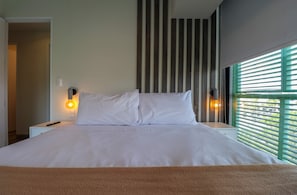 A neatly made bed with white linens, two bedside lamps, and a window with horizontal blinds. - w* | Plaza Stays 2BR with Balcony in San Isidro (San Isidro)