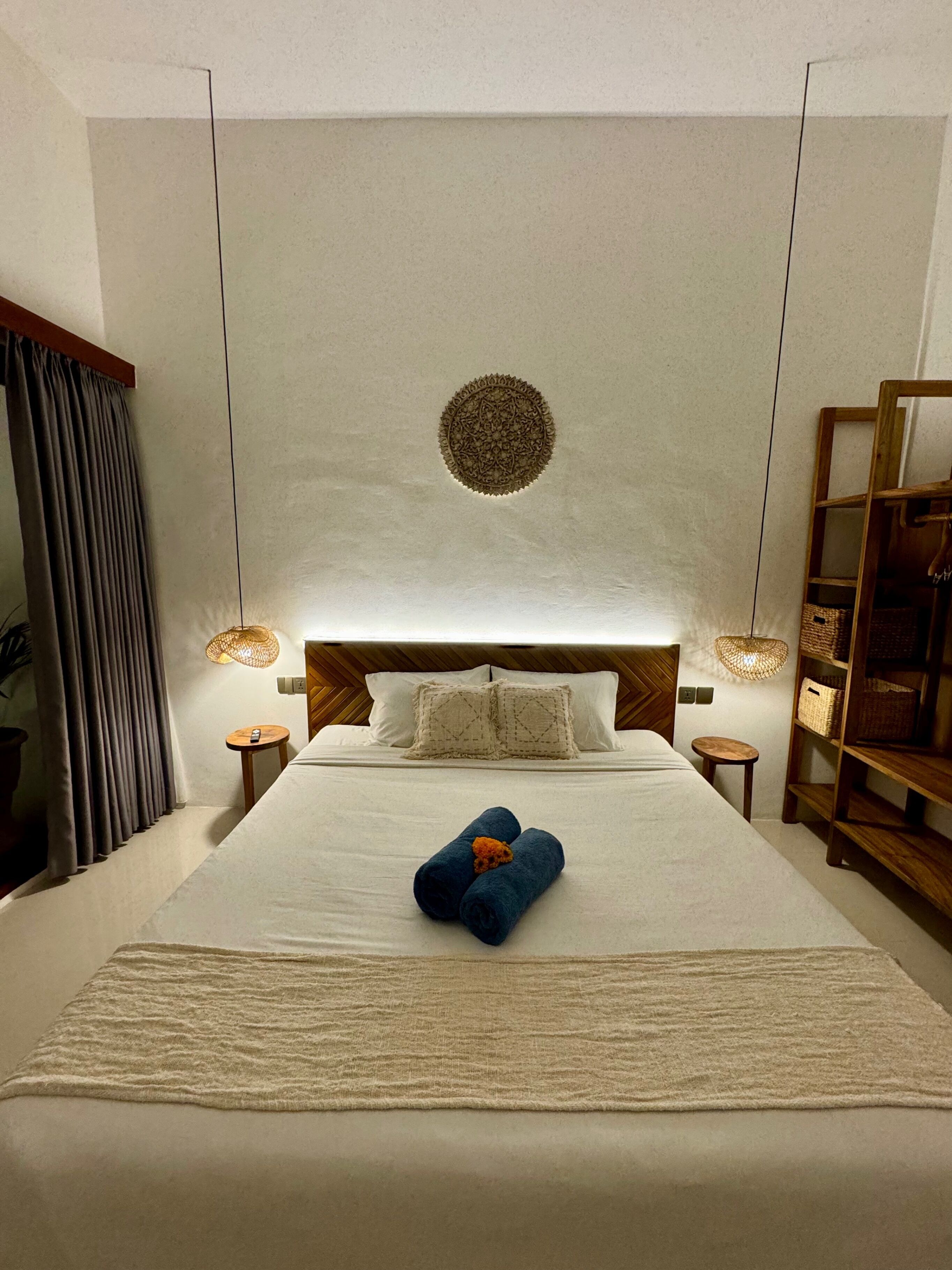 A hotel room with a large bed, two bedside tables, a wooden headboard, a decorative ceiling medallion, and a built-in bookshelf.