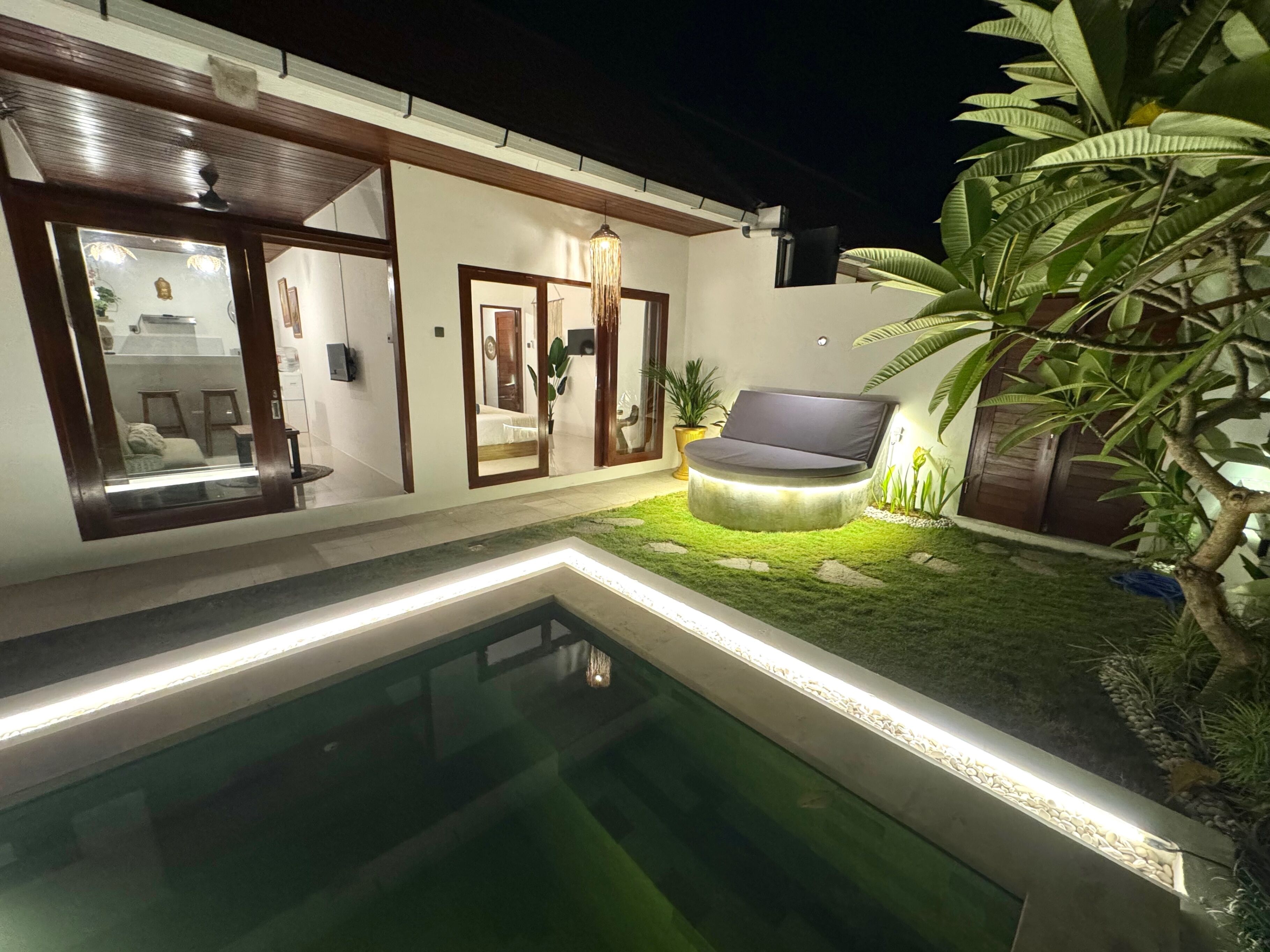 A modern house with a swimming pool, a garden with a circular seating area, and a large mirror reflecting the interior.
