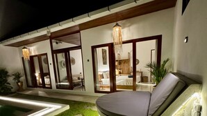 Et moderne udendørs opholdsområde med pool, siddeplads med polstret bænk og en godt oplyst indgang.