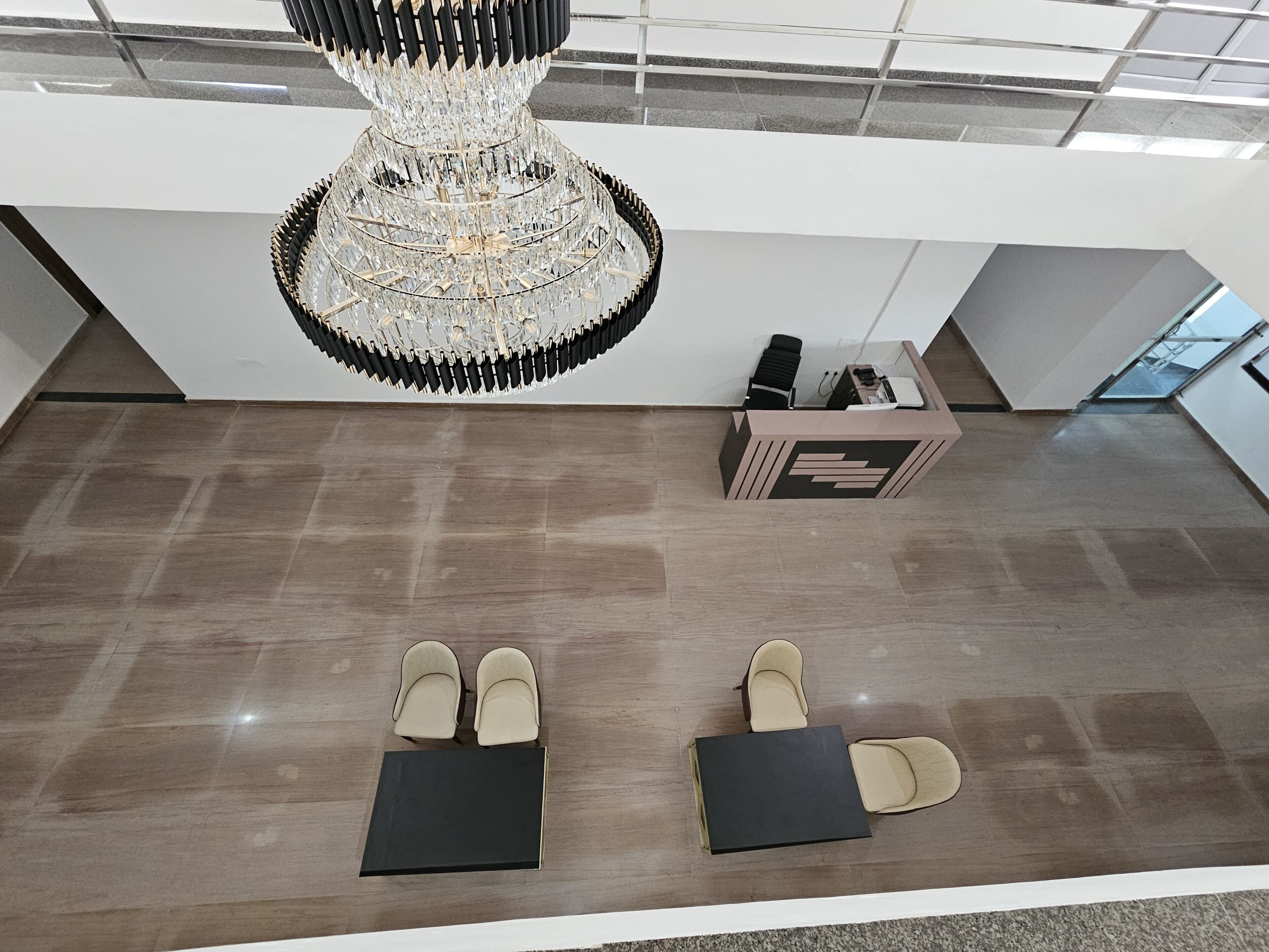 A modern interior with a large chandelier, two pairs of beige shoes on the floor, and a reception desk.