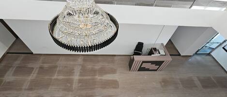 A modern interior with a large chandelier, two pairs of beige shoes on the floor, and a reception desk.