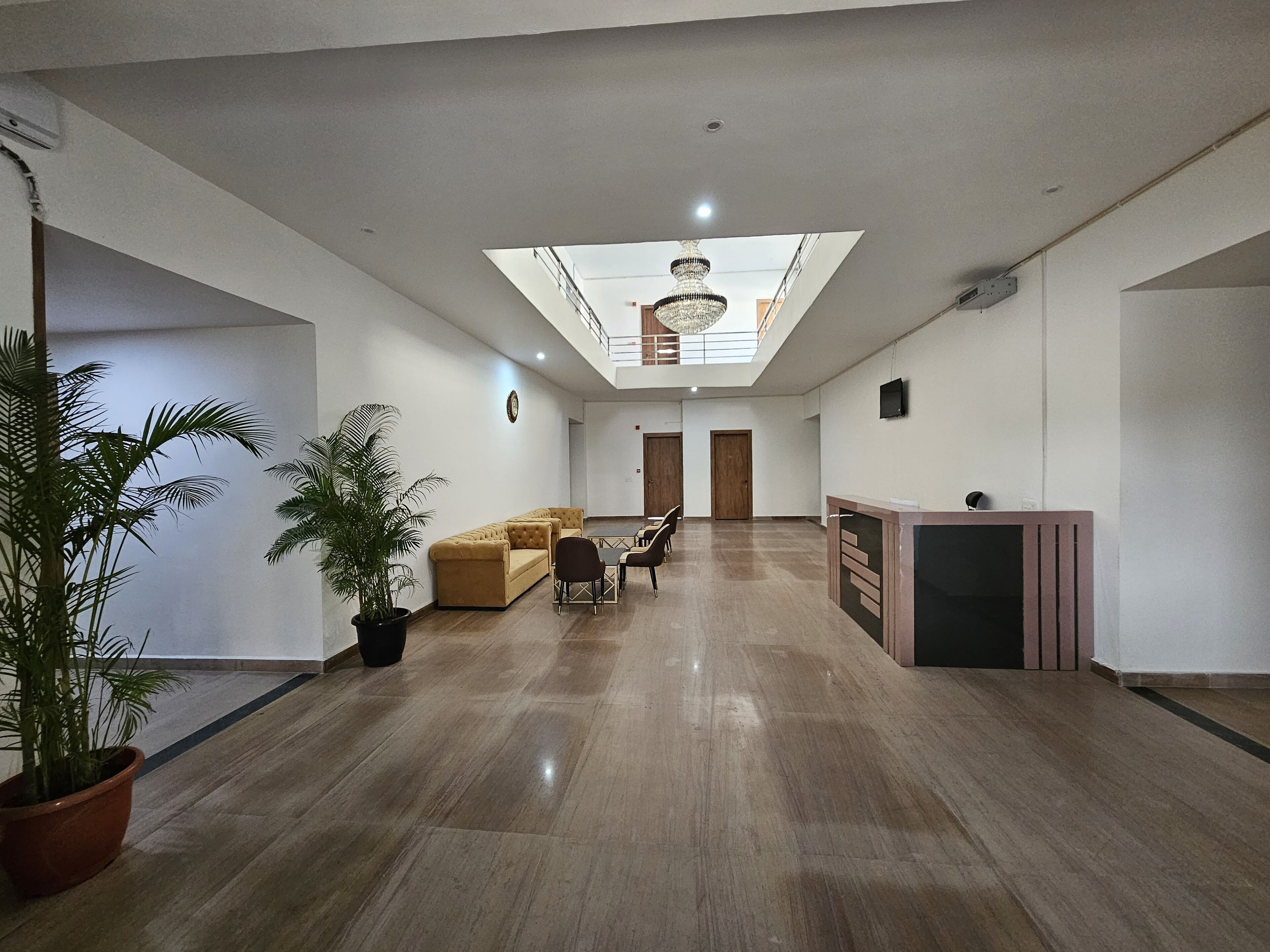 A spacious, well-lit room with a high ceiling, a central seating area with a sofa and chairs, a reception desk, and a large potted plant.