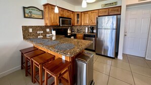 A kitchen with wooden cabinets, a stainless steel refrigerator, granite countertops, and a built-in island with stools. - GV 5317 Golf Course View - Welcome To Paradise (Fort Pierce)