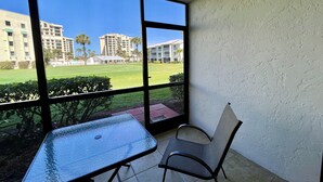 A balcony with a glass table and chair, overlooking a grassy area with buildings in the background. - GV 5317 Golf Course View - Welcome To Paradise (Fort Pierce)