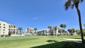 A golf course with a clear sky, palm trees, and modern buildings in the background. - GV 5317 Golf Course View - Welcome To Paradise (Fort Pierce)