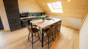 A modern kitchen with a wooden ceiling, a dining table with four chairs, and a skylight. - LE Grenier DU Jean (Sancey)