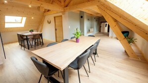 A spacious dining area with a long wooden table and modern chairs, a small window, and a sloped ceiling with exposed beams. - LE Grenier DU Jean (Sancey)