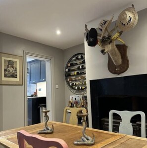 A dining area with a wooden table, chairs, and a decorative wall with a wine rack and a mounted hat. - 3 Bed Home - Sleeps 6, Garden, Pets and Very Central (Guildford)