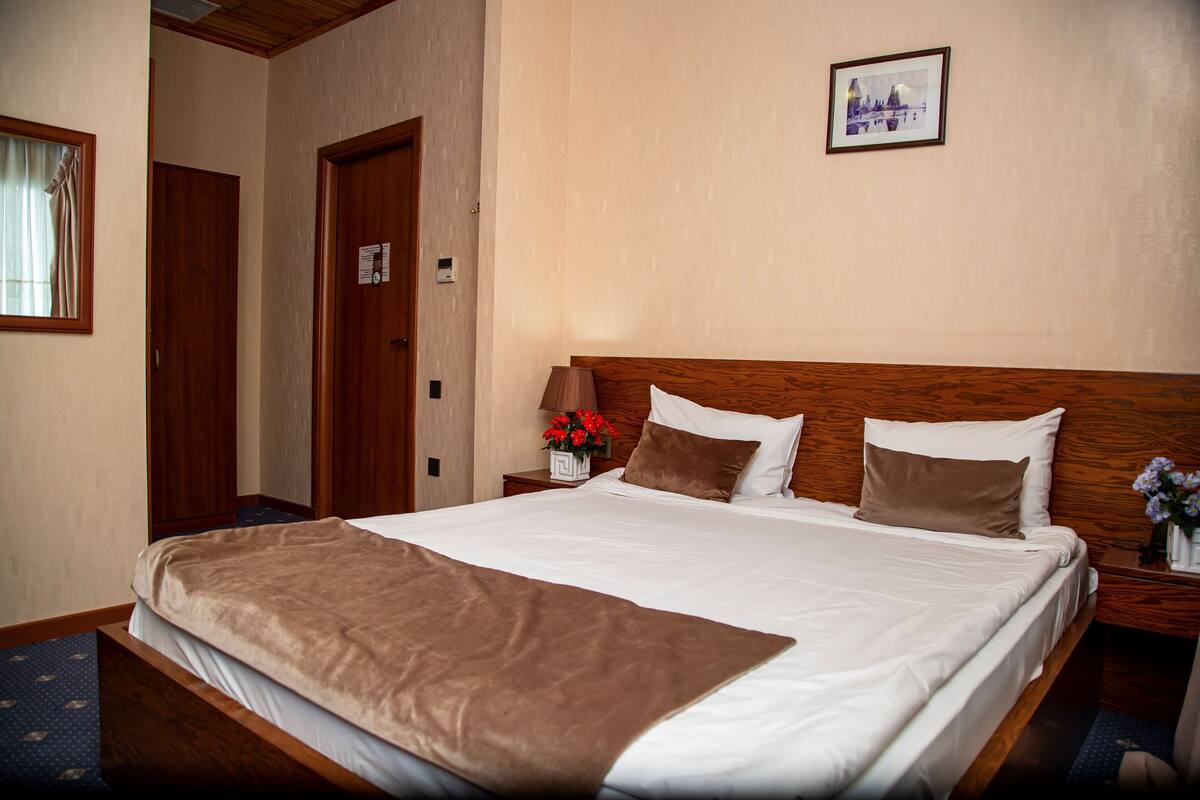 A hotel room with a large bed, wooden headboard, and a nightstand with a vase of flowers.