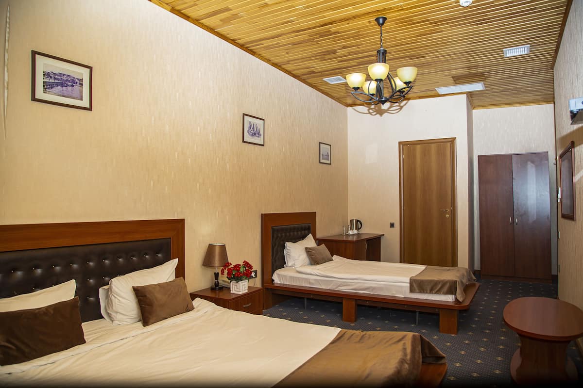 A hotel room with two beds, wooden headboards, a chandelier, and a small round table.