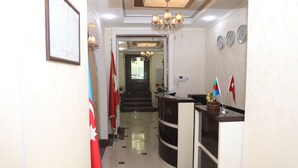A reception area with a reception desk, a chandelier, and flags on the walls. - Port Hotel (Baku)