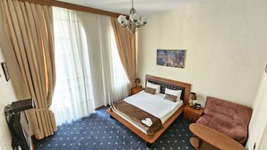 A hotel room with a large bed, a desk, a chair, a desk lamp, and a painting on the wall. - Port Hotel (Baku)