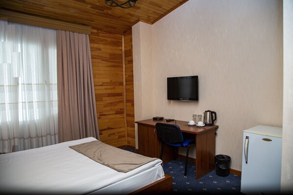 A hotel room with a bed, a desk with a chair, a television, a small refrigerator, and a trash bin. - Port Hotel (Baku)