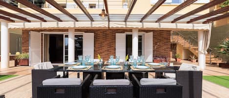 An outdoor patio with a covered dining area, wicker furniture, and a brick wall in the background.