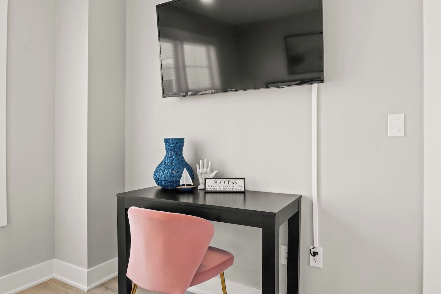 A modern room with a black TV mounted on the wall, a small black table with decorative items, and a pink chair.