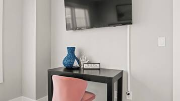 A modern room with a black TV mounted on the wall, a small black table with decorative items, and a pink chair.