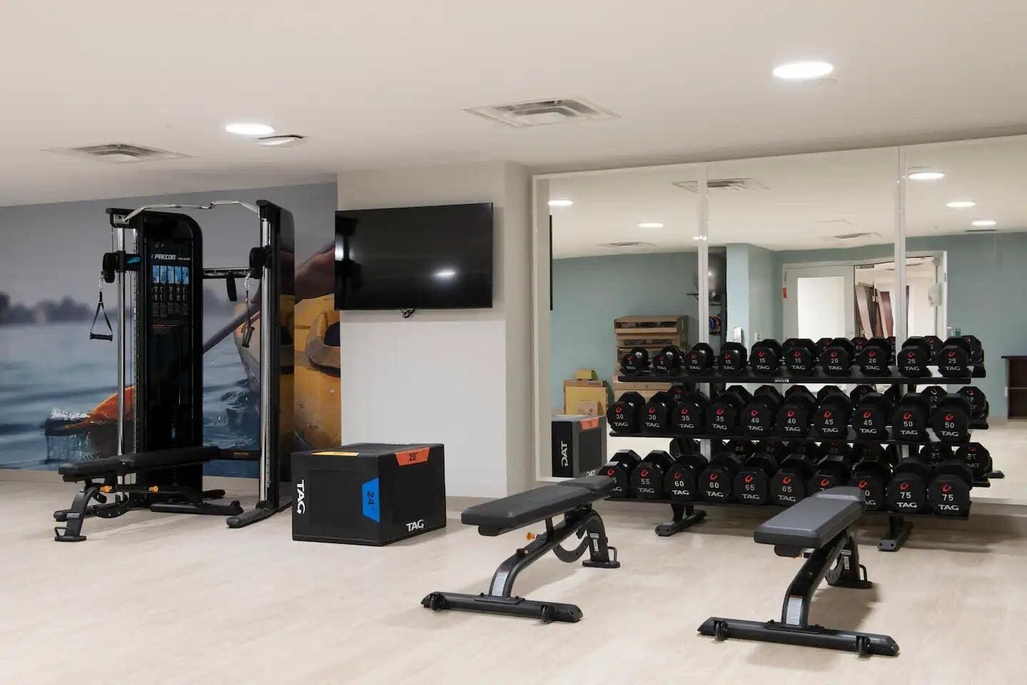 A gym with weightlifting equipment, a bench, and a wall-mounted TV.