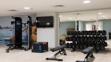 A gym with weightlifting equipment, a bench, and a wall-mounted TV.