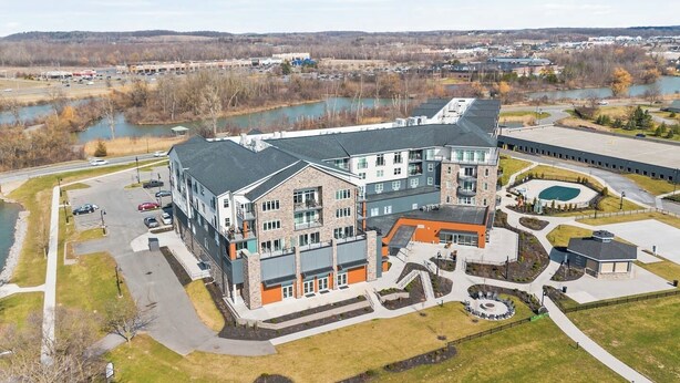 A multi-story building with a parking lot, a swimming pool, and a landscaped area with a small bridge. - Canandaigua Condo w/ Restaurant and Pool/Hot Tub (Canandaigua)