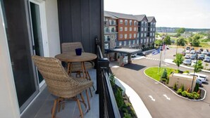A balcony with wicker chairs and a table, overlooking a parking lot and buildings. - Canandaigua Condo w/ Restaurant and Pool/Hot Tub (Canandaigua)
