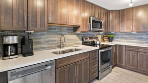 A modern kitchen with dark wood cabinets, stainless steel appliances, and a tiled backsplash. - Canandaigua Condo w/ Restaurant and Pool/Hot Tub (Canandaigua)