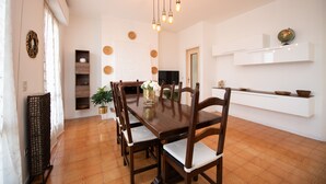 A dining area with a wooden table and chairs, a hanging light fixture, and a white shelf with decorative items. - Villa Torchio (Manerba del Garda)