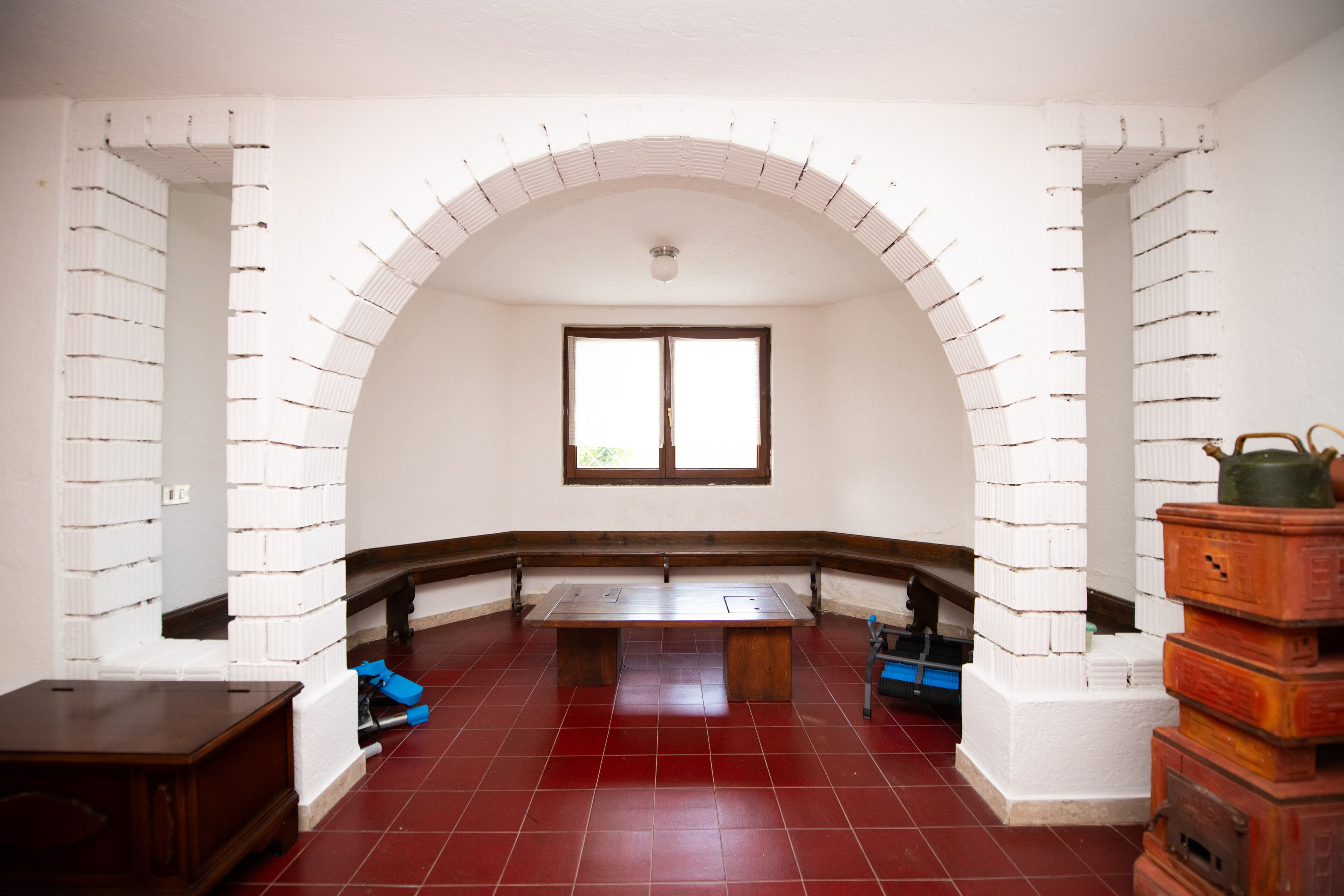 Una habitación con piso de baldosas rojas, un banco de madera y una ventana.