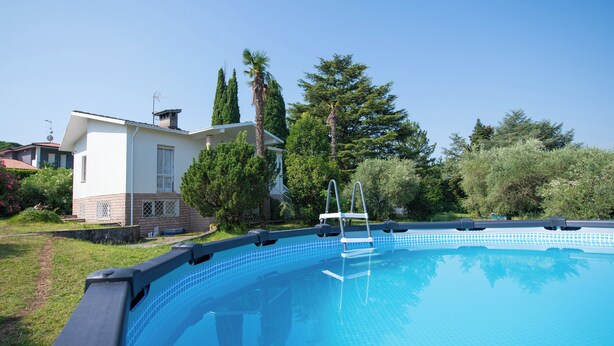 A swimming pool with a clear blue water surface, surrounded by a grassy area and trees. - Villa Torchio (Manerba del Garda)
