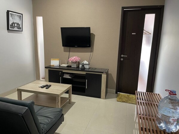 Una sala de estar con televisor, mesa de centro, sofá, mueble y una botella de agua.