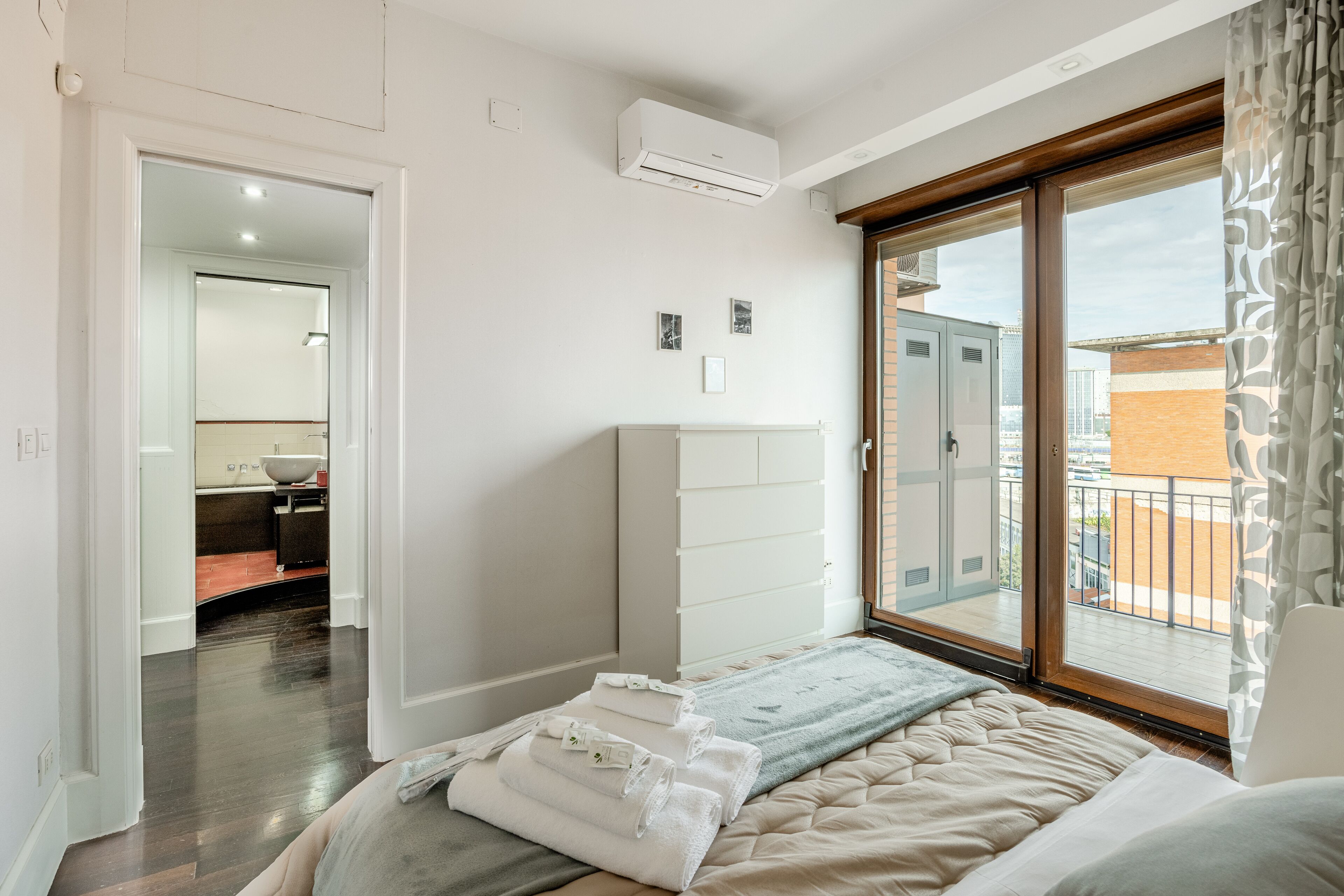 Una habitación de hotel con cama, ventana con vistas, armario y baño a la vista a través de una puerta abierta.