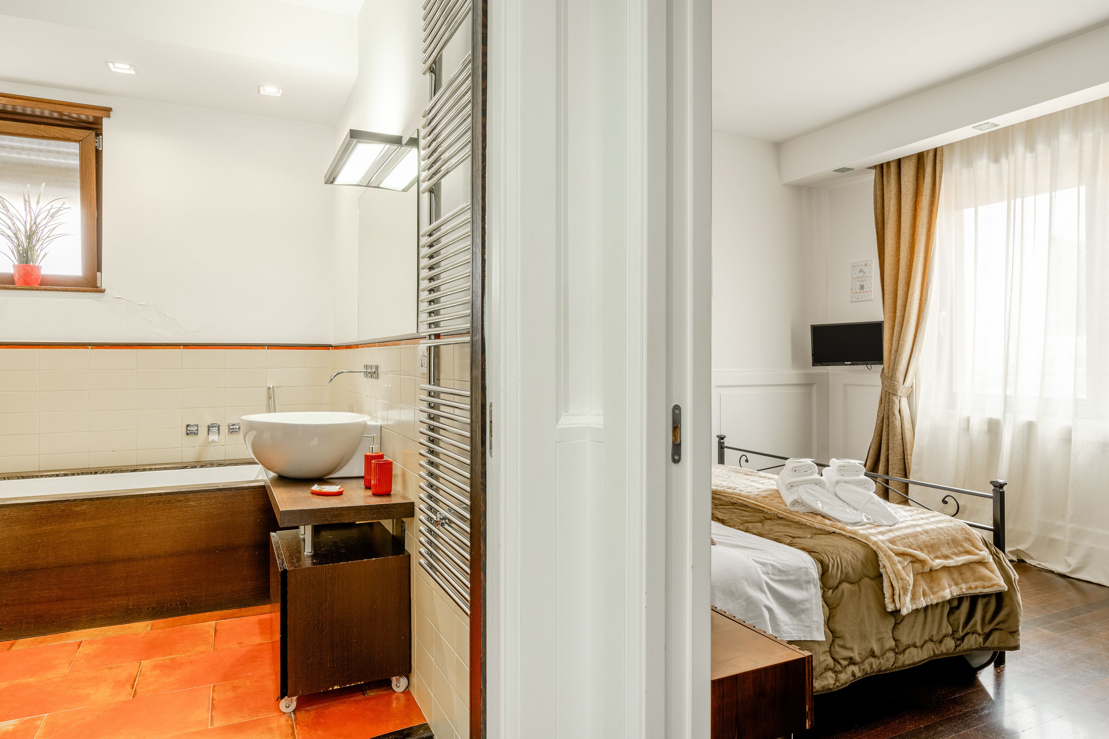 A hotel room with a large white sink, a wooden vanity, a bed with a beige blanket, and a television on a stand.