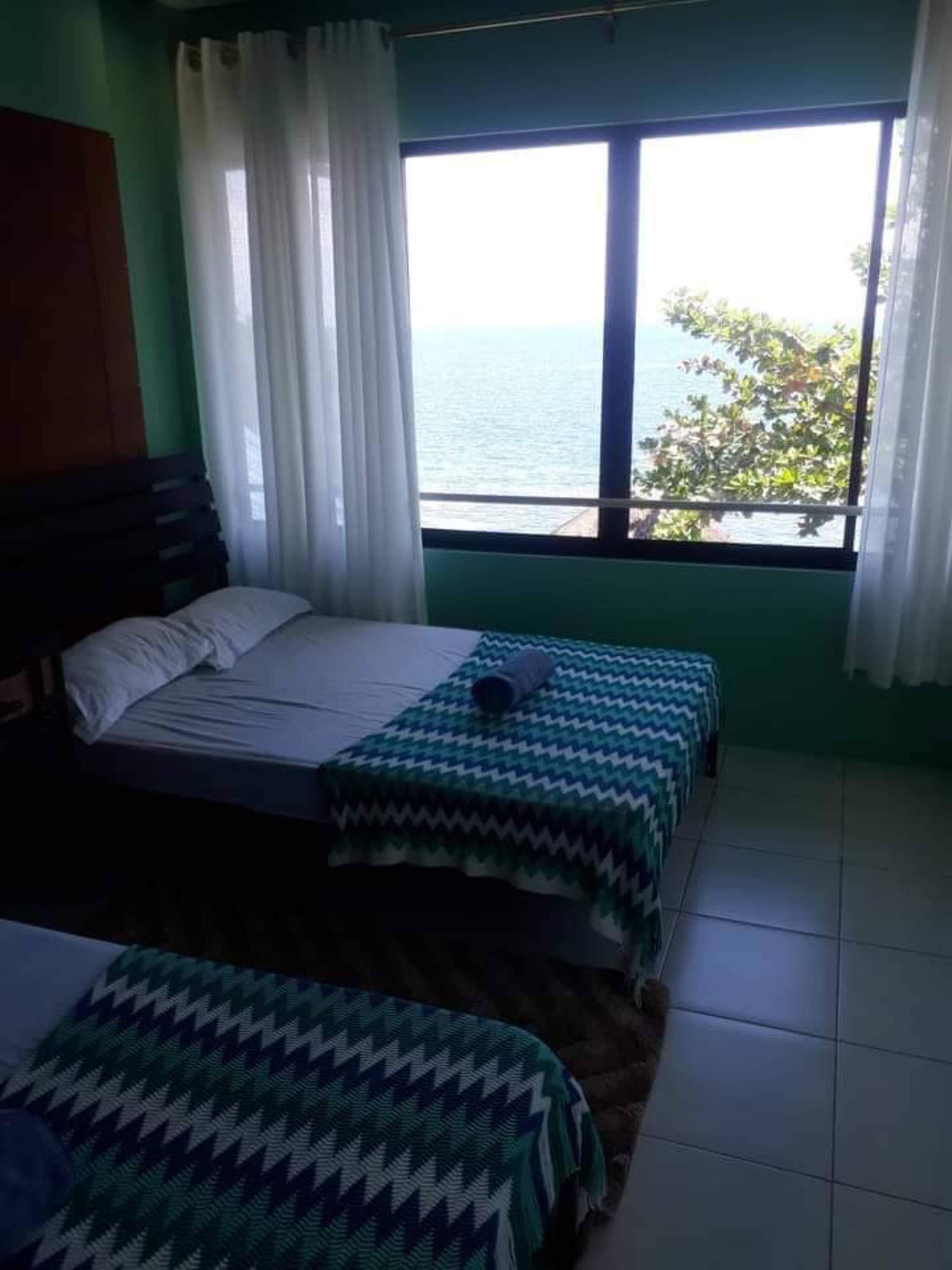 Ein Zimmer mit einem Bett, einem Fenster mit Meerblick und einem Vorhang.