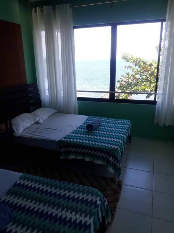 A room with a bed, a window with a view of the sea, and a curtain.