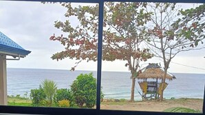 A kitchen with a sink and a window overlooking a beach with a thatched-roof structure. - Seaheart Guesthouse (Dauis)