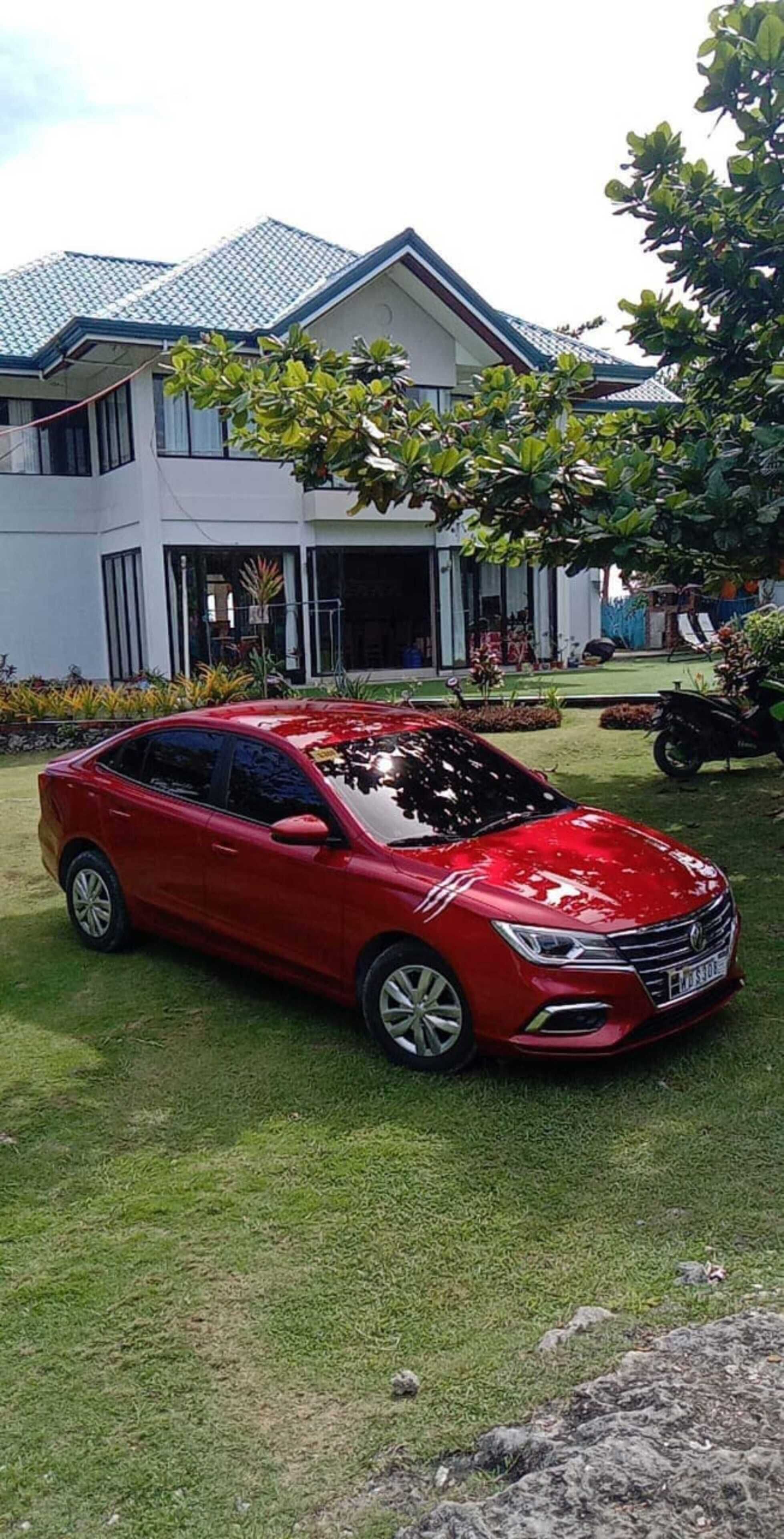 A red car parked in front of a modern two-story building with a tiled roof.