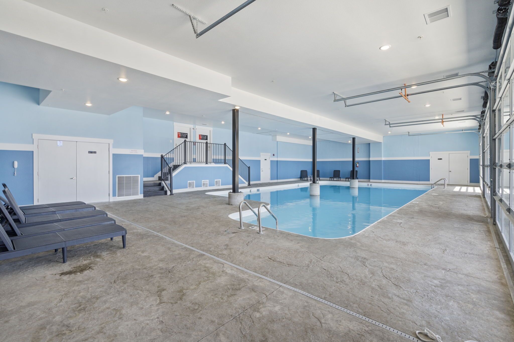 Une piscine intérieure dotée d’un espace à eau claire, d’un escalier et de chaises longues.