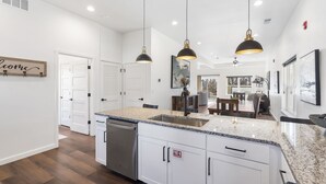 Une cuisine moderne avec des meubles blancs, des plans de travail en granit et des luminaires suspendus.