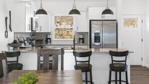 Une cuisine moderne avec des meubles blancs, des appareils en acier inoxydable et un grand îlot central doté de tabourets de bar.