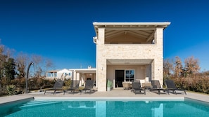 Une maison moderne dotée d’une piscine, d’un espace salon extérieur et d’une façade en pierre.