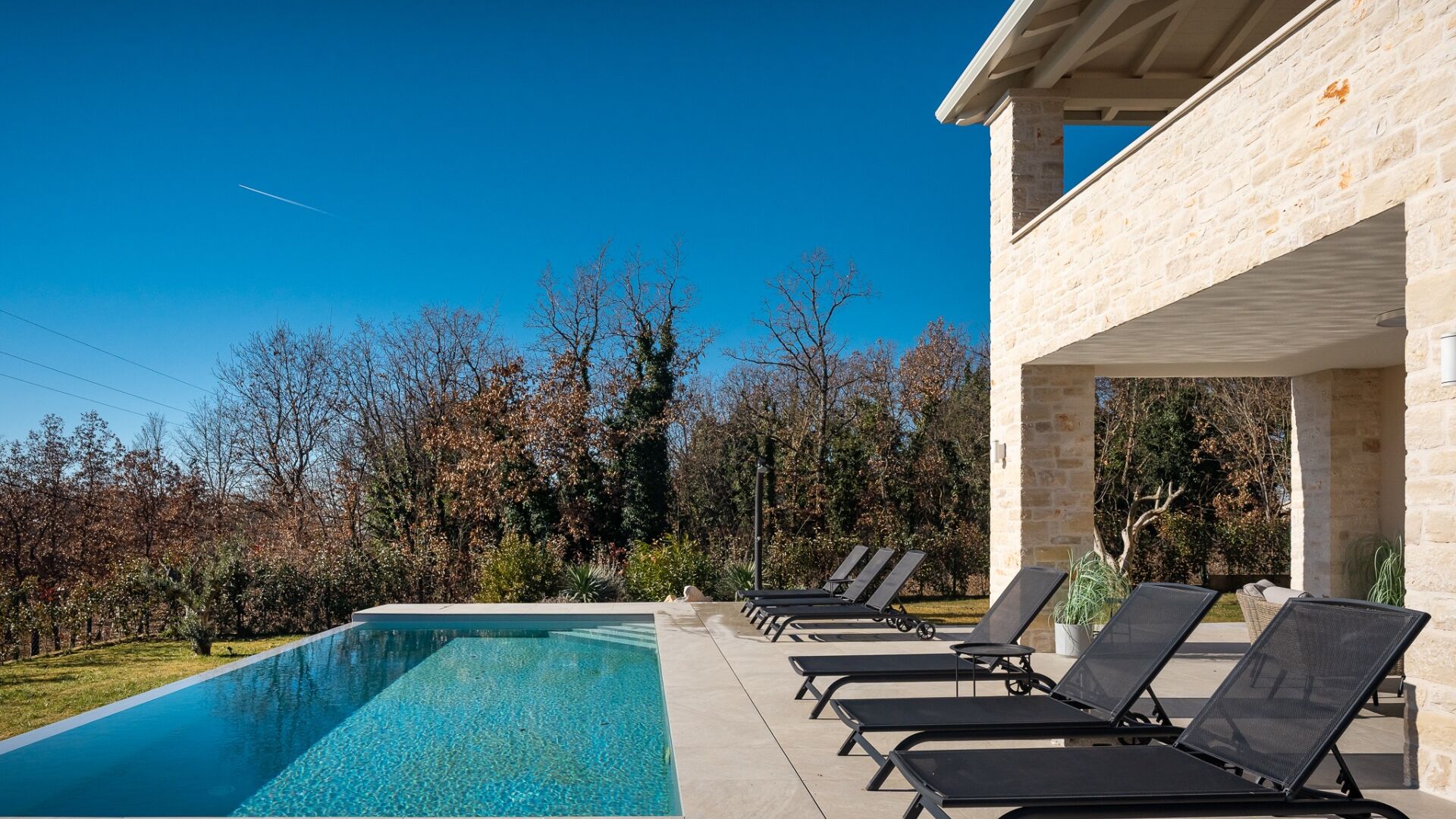 A swimming pool with lounge chairs, a stone building, and trees in the background.