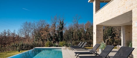 A swimming pool with lounge chairs, a stone building, and trees in the background.